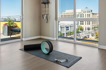 A yoga mat and a rolled-up mat are on the floor of a room with a view of the city.